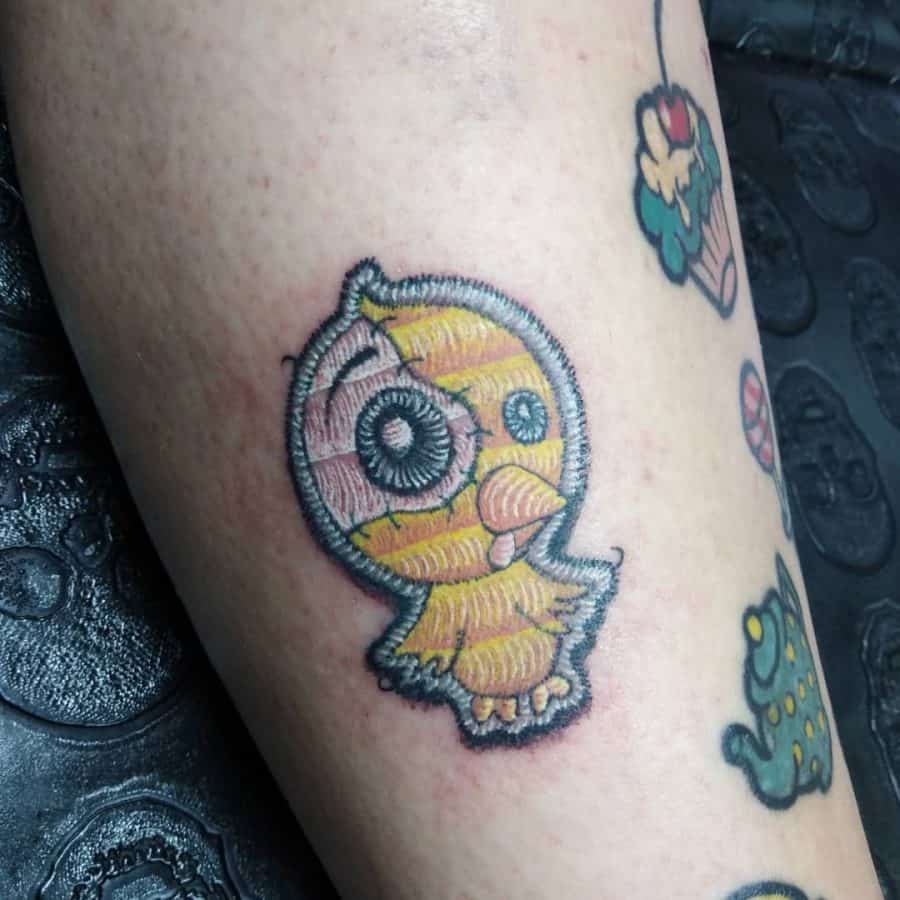 Adorable embroidery-style chick tattoo featuring pastel yellow and pink hues with a sewn-on patch look.