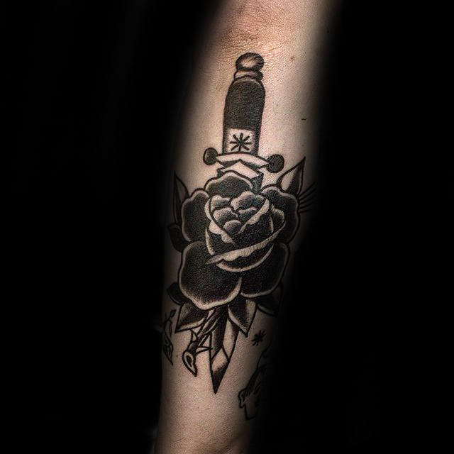 Tattoo of a dagger and rose with leaves on a forearm