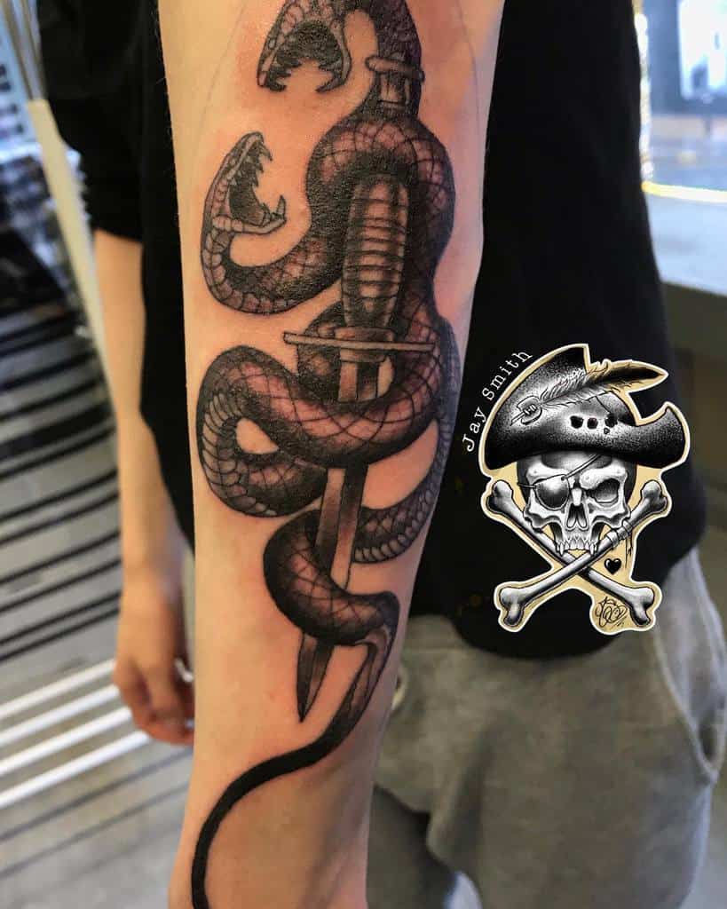 Realistic tattoo of a coiled snake wrapped around a dagger, with detailed scales and fangs, placed on the forearm