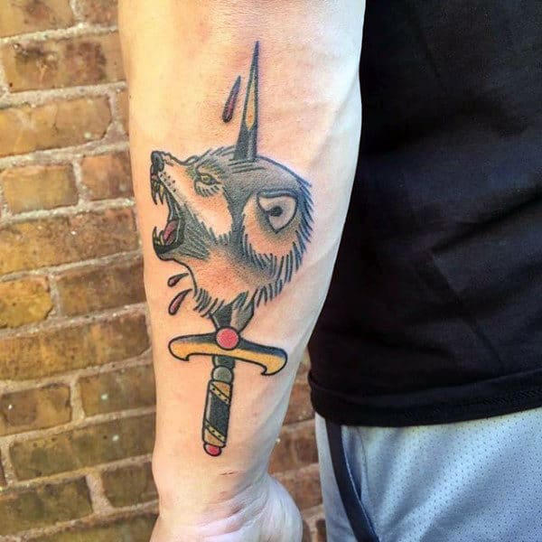 Tattoo of a wolf head pierced by a dagger on an inner forearm