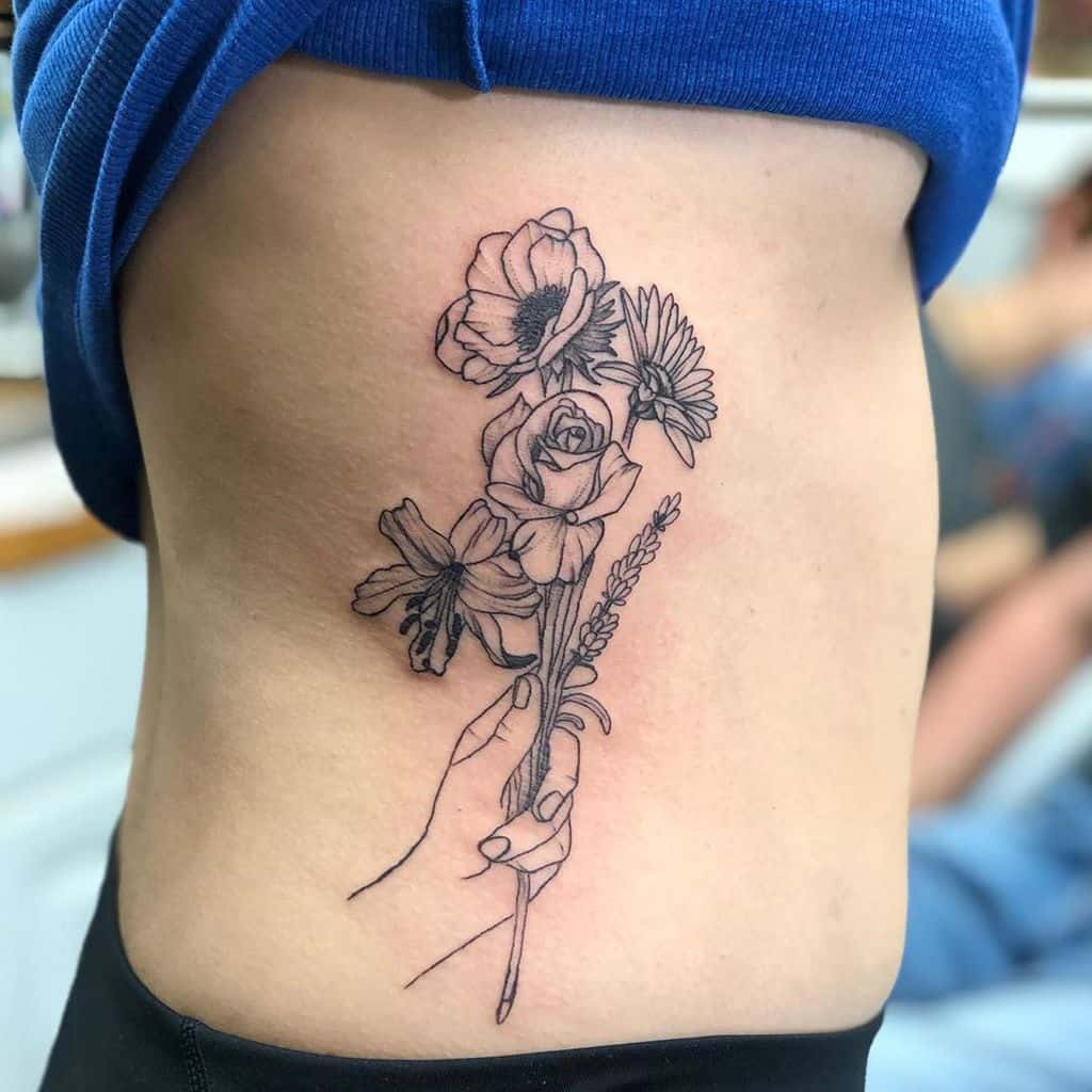Rib tattoo black and grey fine line shading hand holding daisy flower bouquet