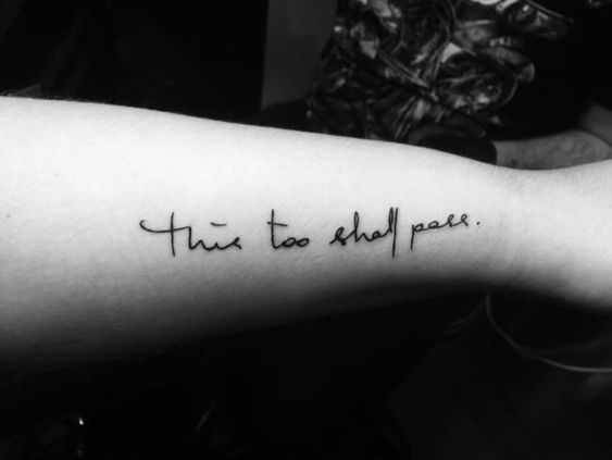 "This too shall pass" tattoo in cursive on the forearm.