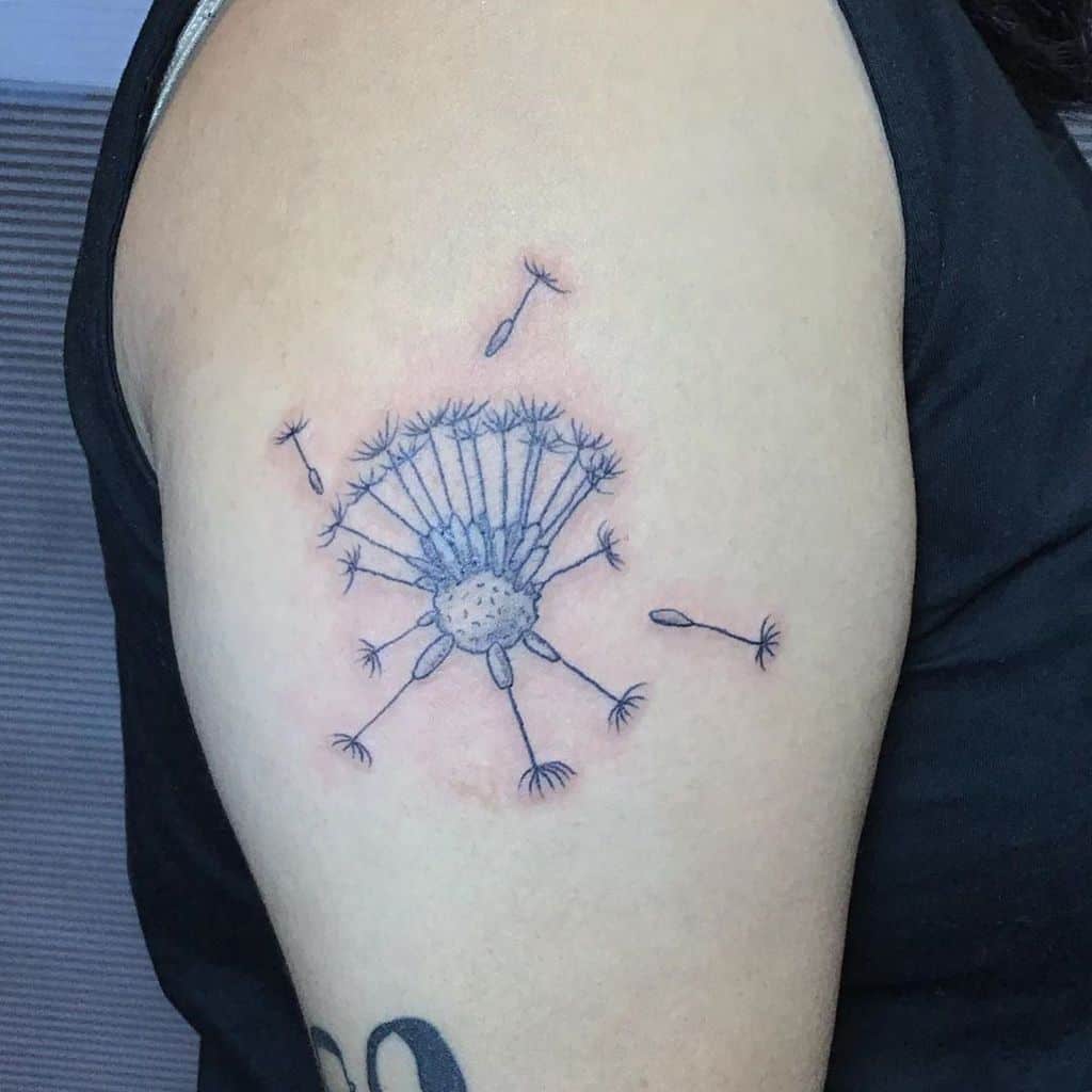 This tattoo showcases a delicate dandelion with seeds gently floating away. The design, with soft colors and fine lines, symbolizes freedom and transformation, placed beautifully on the shoulder.
