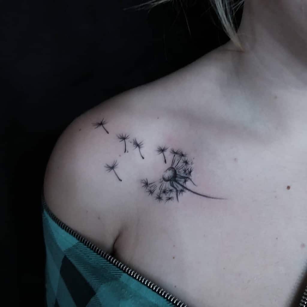 Fine-line dandelion tattoo on the shoulder with seeds floating away, symbolizing freedom, dreams, and new beginnings.