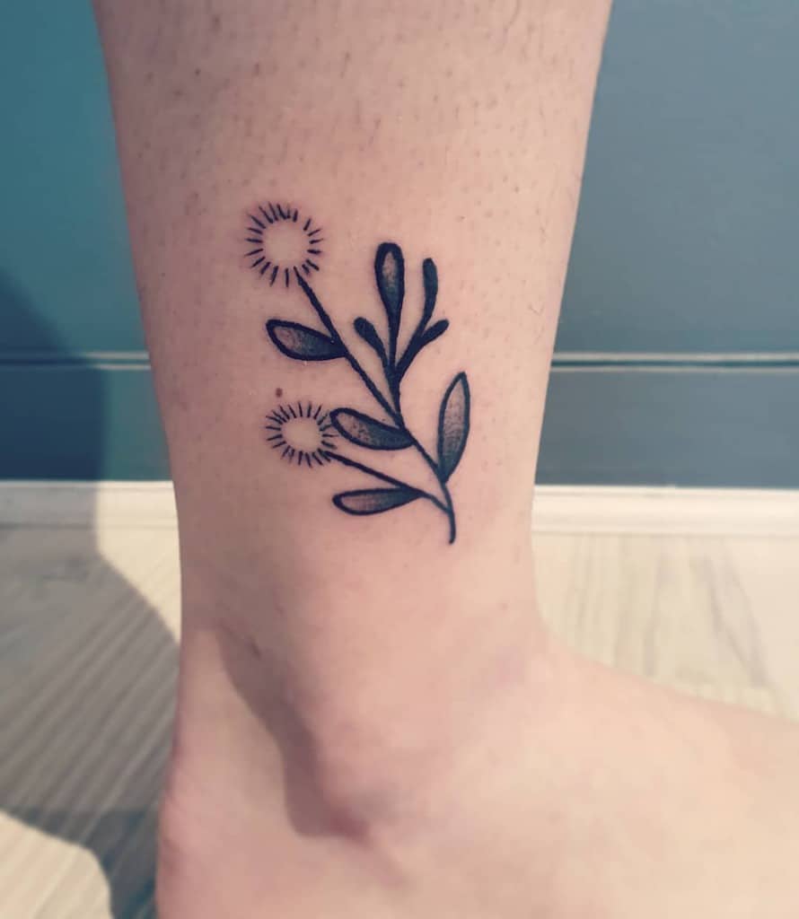 Stylized dandelion tattoo on the ankle with bold leaves and minimal linework, symbolizing growth, strength, and simplicity.