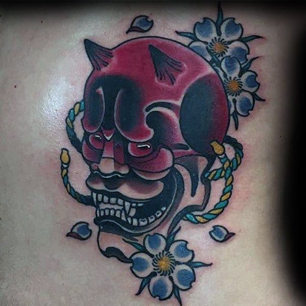 Traditional-style Daredevil mask tattoo with Japanese oni influences, surrounded by blue flowers and decorative rope details.