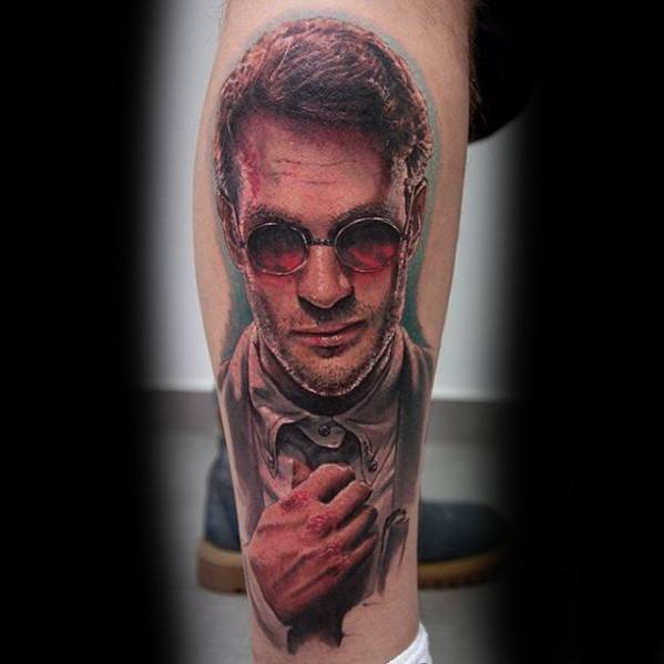 Realistic tattoo of Matt Murdock with red-tinted glasses, bruised face, and intense expression, capturing his dual identity as Daredevil.