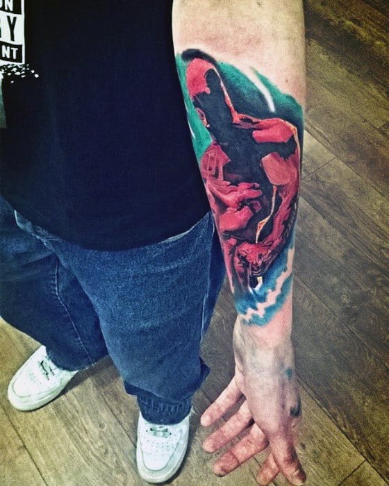 Forearm Daredevil tattoo with dynamic red and black tones, showing him mid-leap against a swirling blue and teal background.