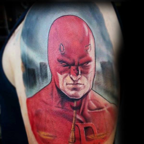 Detailed Daredevil tattoo with a serious expression, vivid red suit, and a moody cityscape background on the upper arm.