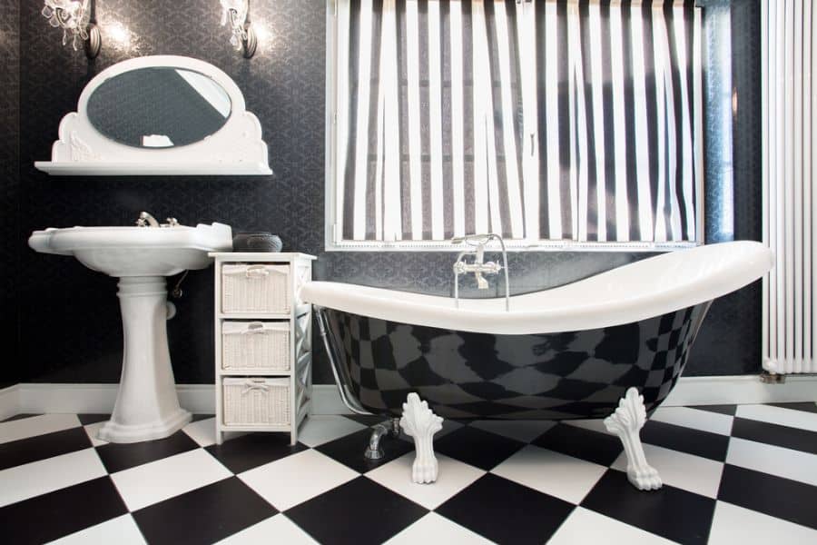 Monochrome bathroom with clawfoot tub, checkered floor, and striped window blinds.