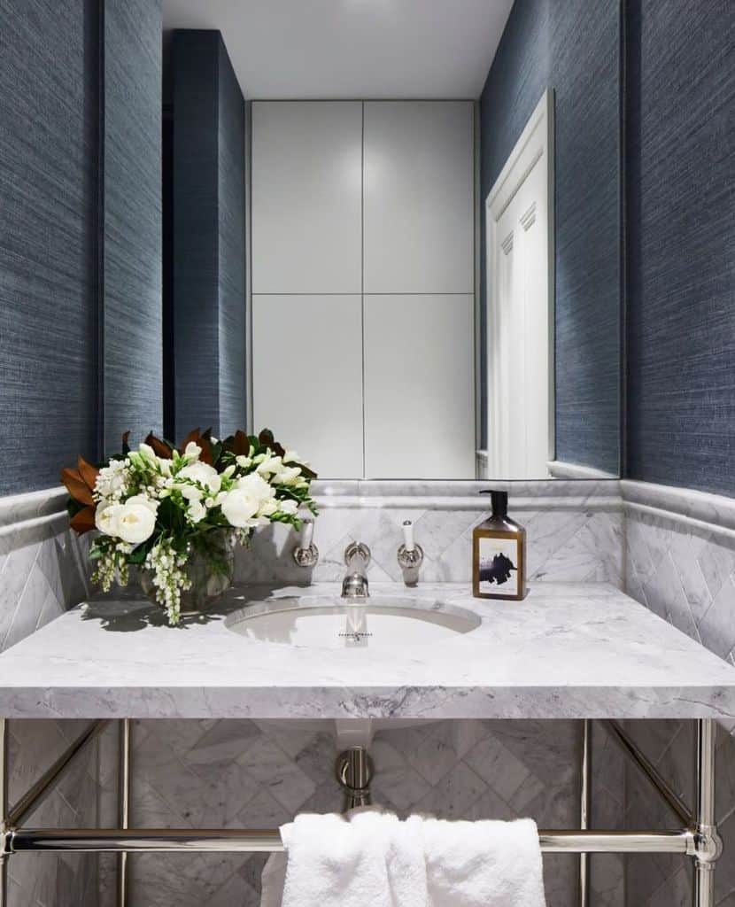 Bathroom with blue textured wallpaper, marble vanity, and floral arrangement.