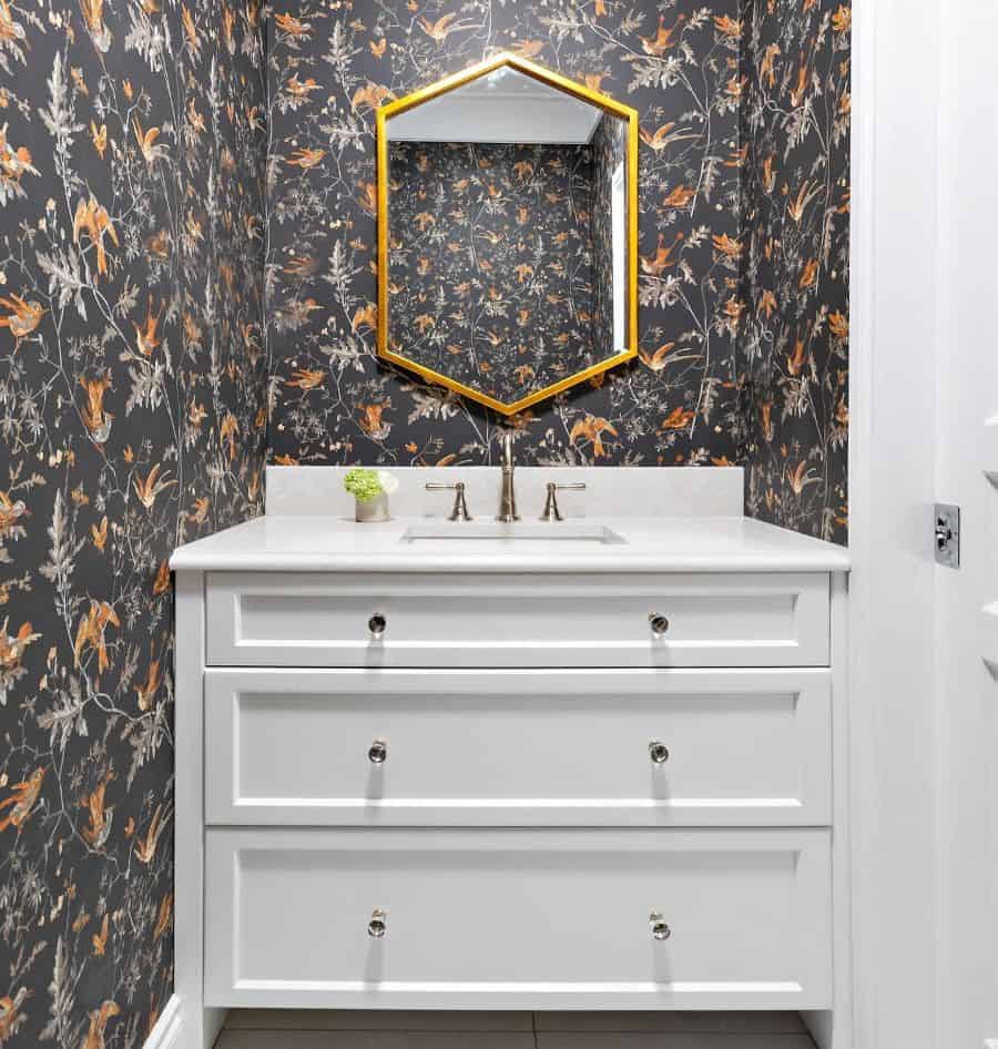 Bathroom with bird-patterned wallpaper, white vanity, and gold hexagonal mirror.