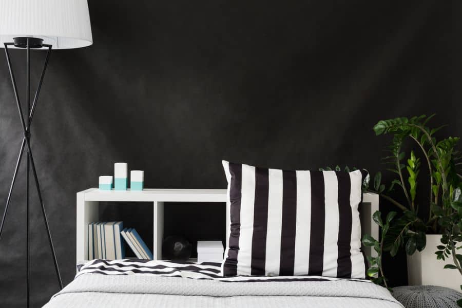 Modern bedroom with black walls, striped pillow, white shelving, and indoor plants.
