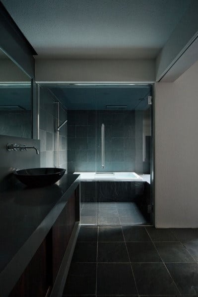 Modern bathroom with dark tiles, a glass-walled shower, and a black vessel sink
