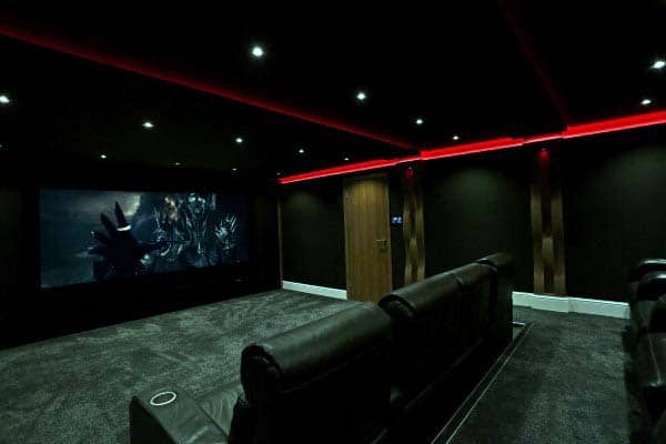 A home theater room with leather recliners, red LED lighting, and a large screen showcasing an epic movie scene