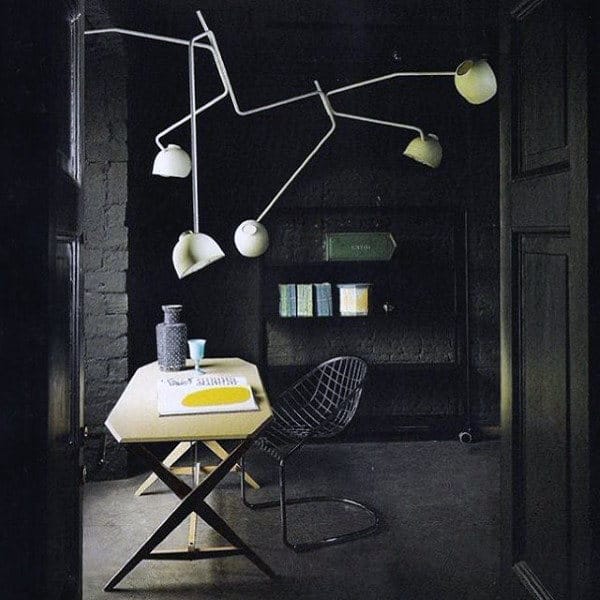 Modern, dark room with a geometric table, wire chair, and unique ceiling light fixture