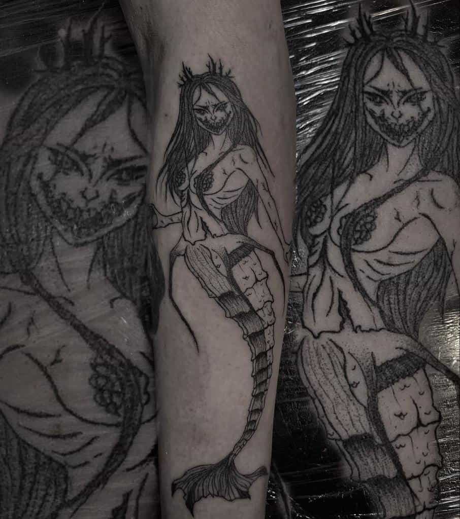Dark horror-themed tattoo of a sinister mermaid with a skeletal grin, stitched-together tail, and eerie crown, designed in a macabre style.