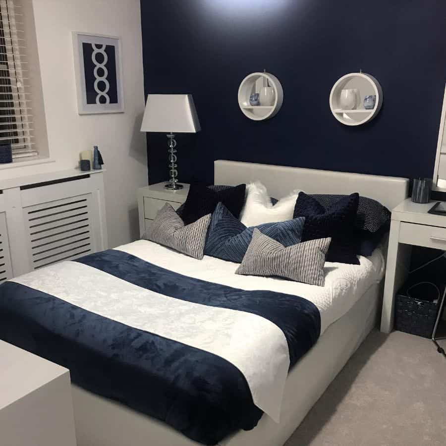 Modern bedroom with dark blue accent wall, white bed, and navy and gray pillows.