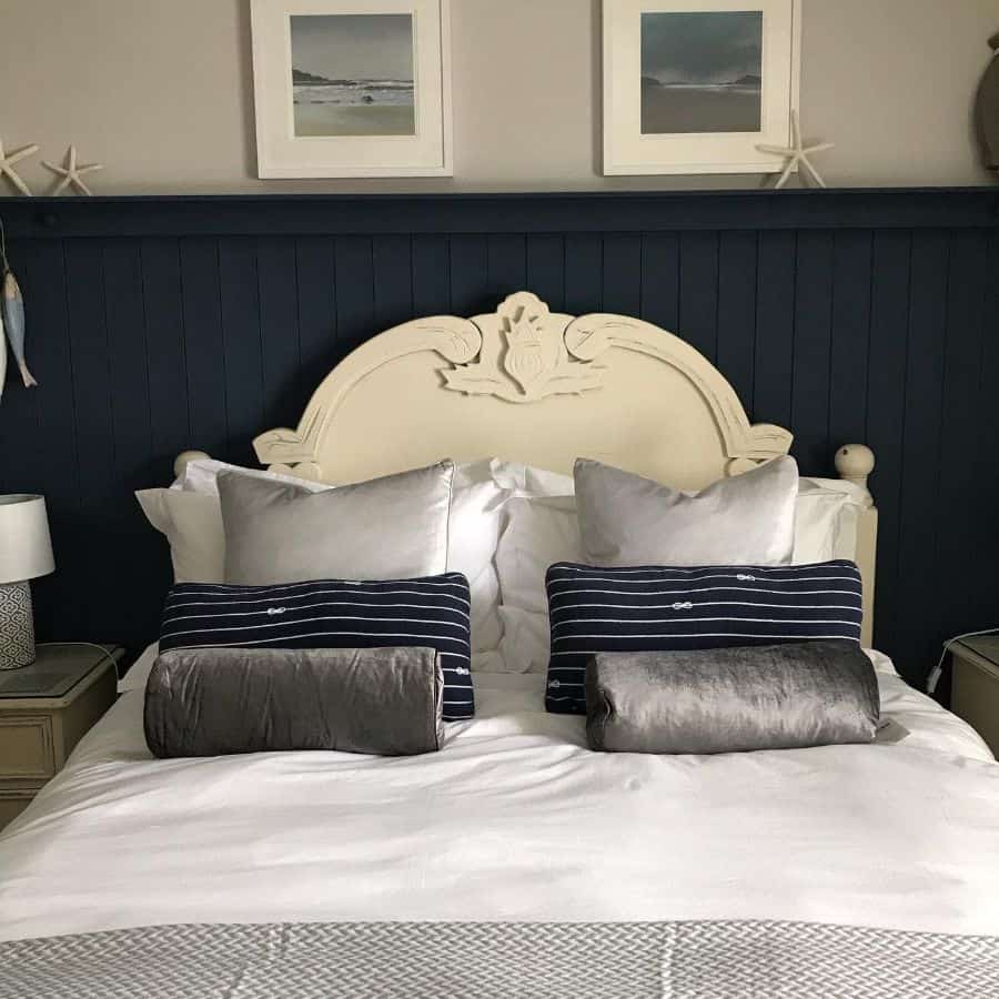 Classic bedroom with dark blue paneled wall, cream headboard, and striped pillows.