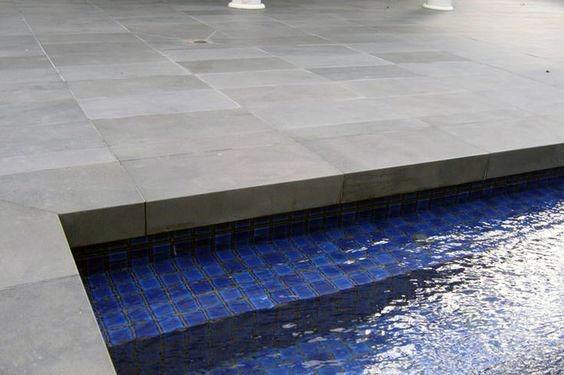 Dark blue mosaic tiles lining a sleek pool edge, paired with a modern grey stone deck.
