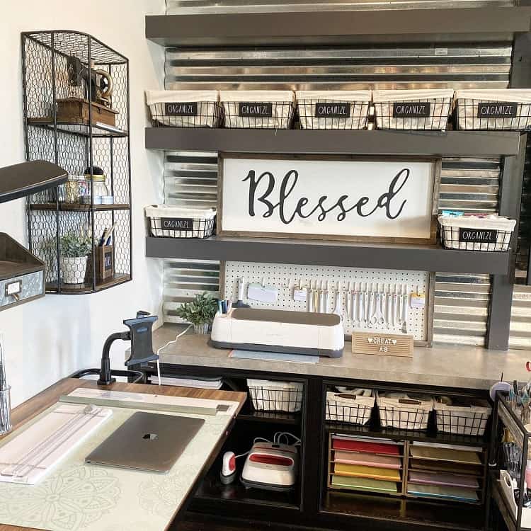 Organized craft room with "Blessed" sign, shelves, baskets, and a craft machine on a desk