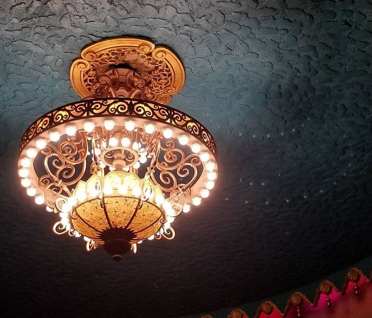 Ornate chandelier with glowing bulbs on a decorative, textured ceiling with intricate patterns
