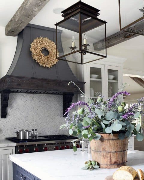 Rustic kitchen with dark range hood, white marble island, wood beam accents, and floral decor.