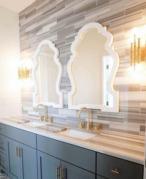 Modern gray vanity with marble countertop, ornate mirrors, and gold fixtures.
