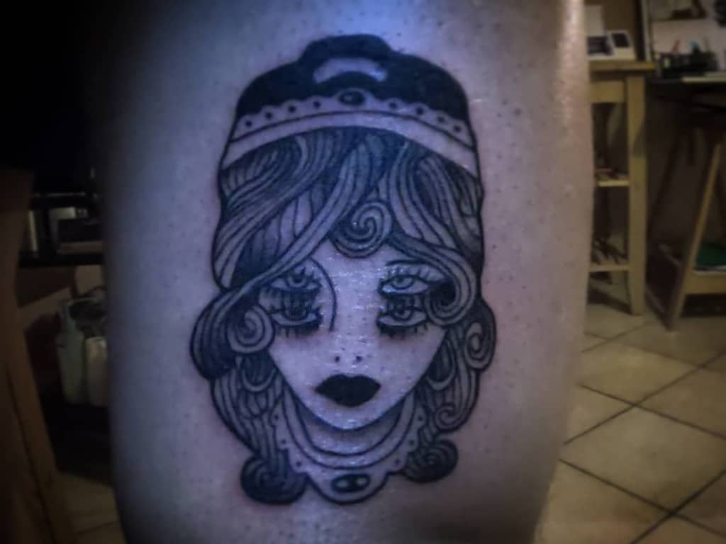 Dark blackwork tattoo of a gypsy woman with hypnotic eyes, bold shading, and intricate hair details on the leg.
