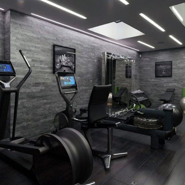 Modern home gym with dark walls, sleek equipment, skylight, and illuminated ceiling lights.
