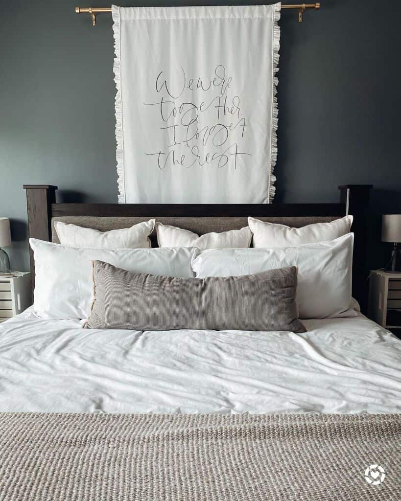 Cozy bedroom with a neatly made bed, layered pillows, and a wall hanging with cursive writing above the headboard