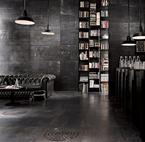 Dark, stylish man cave with a black leather sofa, tall bookshelf, and hanging lights; industrial-chic decor