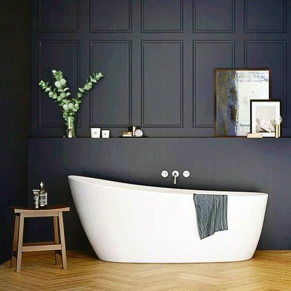 Bathroom with dark navy paneled wall, white freestanding bathtub, and wooden stool.