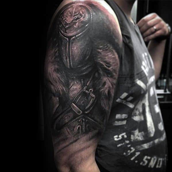Dark Souls upper arm tattoo of a knight in worn armor and fur cloak, rendered in detailed black and grey realism.