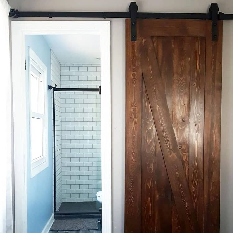 Dark wood sliding barn door leading to a bathroom with white subway tile and black fixtures.