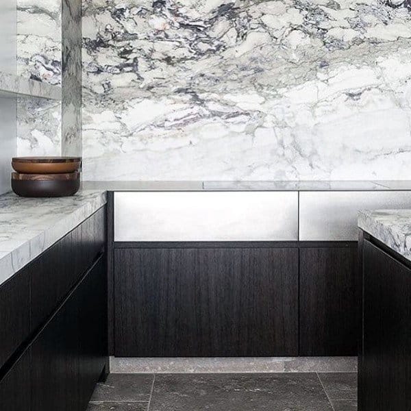 Modern kitchen with dark wood cabinets, marble countertops, and striking marble backsplash.