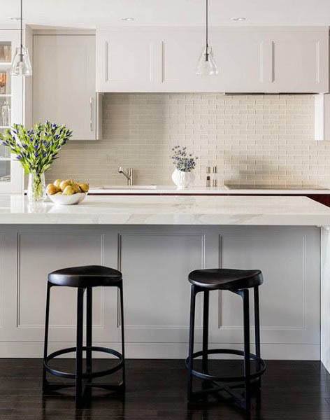 Bright kitchen with white cabinets, marble island, black stools, and subway tile backsplash.