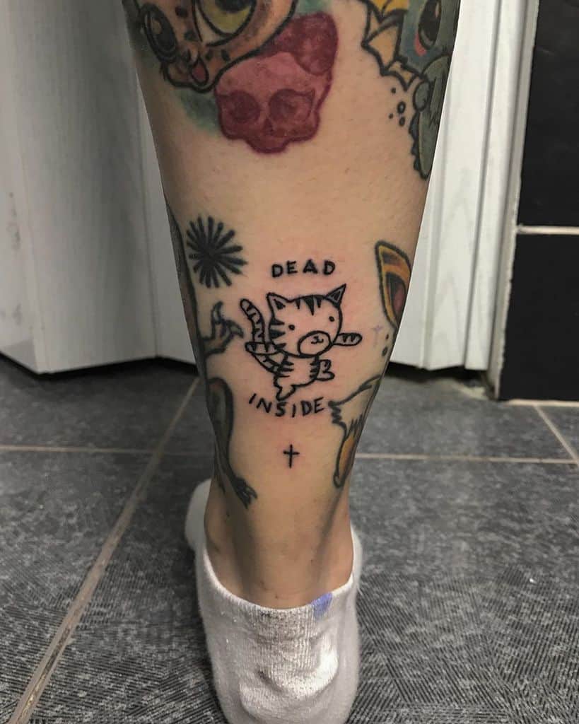 Funny tattoo of a sad cartoon cat floating with angel wings, with 'Dead Inside' written above. A darkly humorous take on exhaustion.