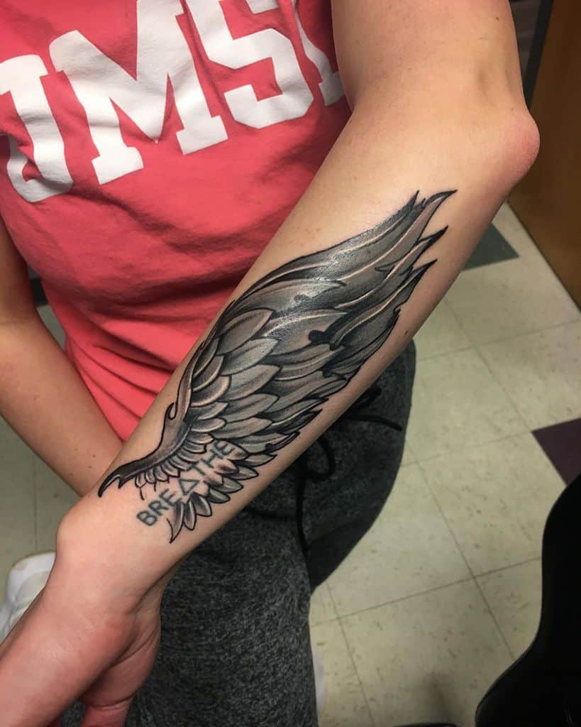 A detailed angel wing tattoo with a text, 'Breathe' below