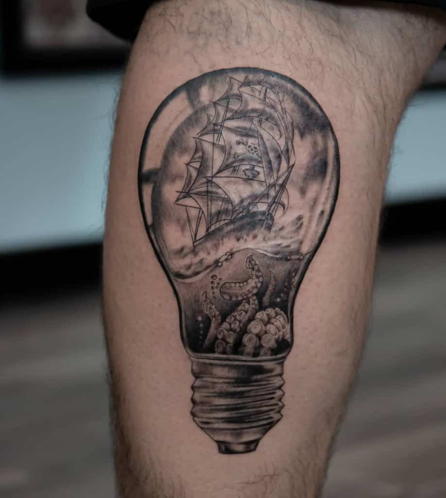 Black and gray tattoo of a lightbulb containing a detailed nautical scene, featuring a pirate ship on stormy ocean with tentacles rising from below