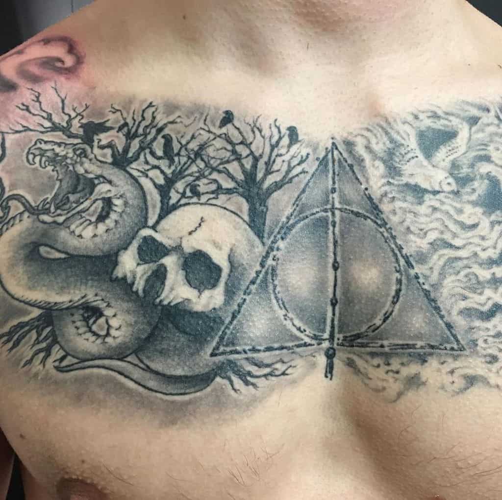 Dark-themed Deathly Hallows chest tattoo featuring a snake, skull, eerie trees, and a misty atmosphere with intricate black and grey shading.