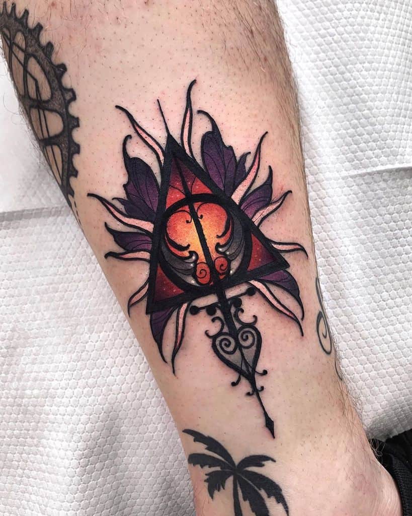Deathly Hallows tattoo with a geometric design, fiery gradient in the center, ornate arrow, and floral elements in deep purple.