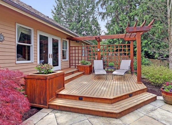 Wooden deck with pergola, lattice privacy screen, planters, and lounge chairs in a garden setting.