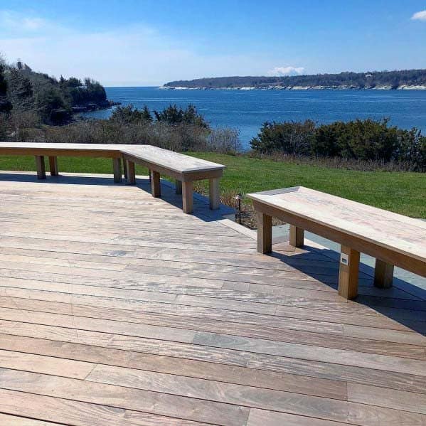 Wooden deck with built-in benches overlooking the ocean and lush greenery under a clear blue sky