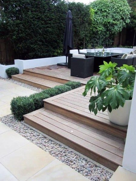 Small wooden deck with steps, modern seating, potted plants, and pebble landscaping.