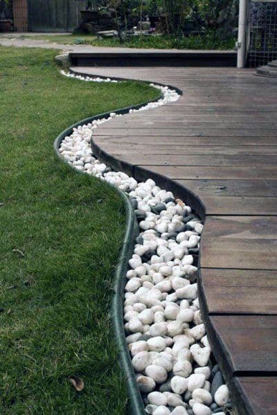 Elegant deck edging with a curved line of white river rocks, neatly contrasting with the green grass and wooden decking
