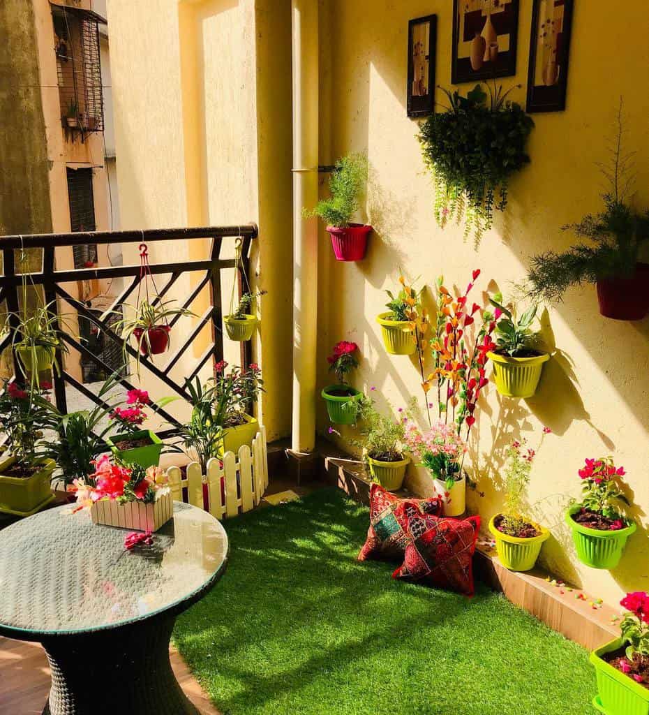 Small balcony garden with colorful hanging planters, artificial grass, and a glass table.