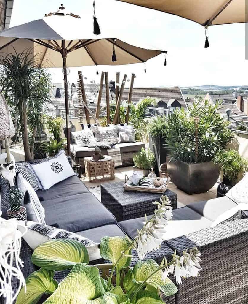 Modern balcony with grey outdoor furniture, plants, and umbrellas, creating a cozy lounge space.