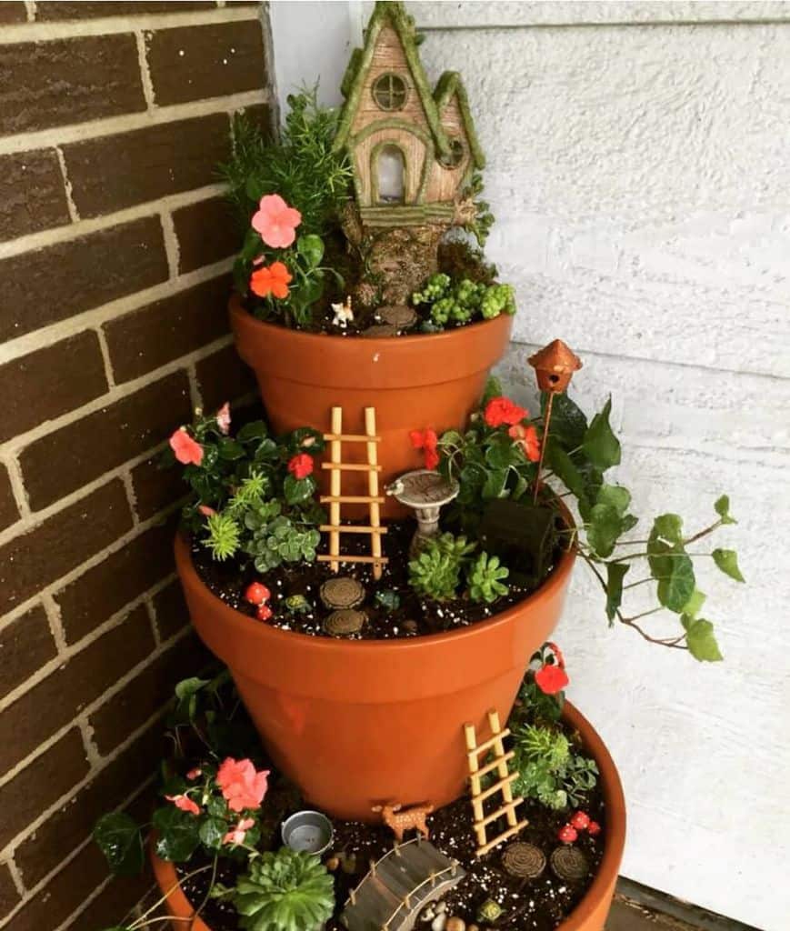 Layered terracotta pots with small plants, flowers, and miniature fairy garden decorations.