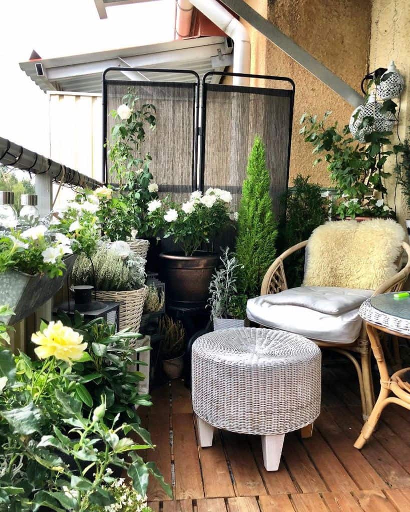 Cozy balcony garden with wicker furniture, potted plants, and a privacy screen.